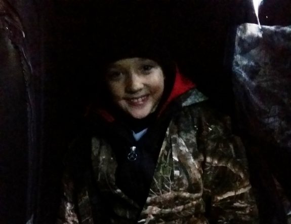 Huddled in the corner of the small blind, Zachery braces against the howling wind on opening day of deer season.