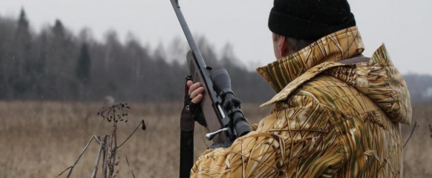 male-hunter-near-tall-grass-and-trees-with-gun